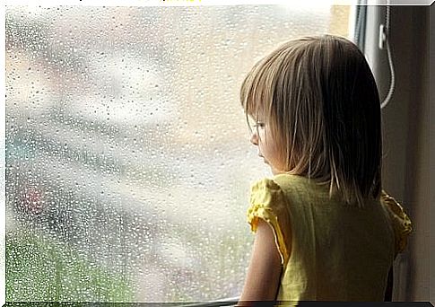 Little girl looks out at rain through window