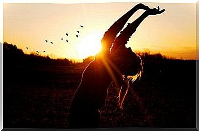 Woman with arms over head in front of sunset