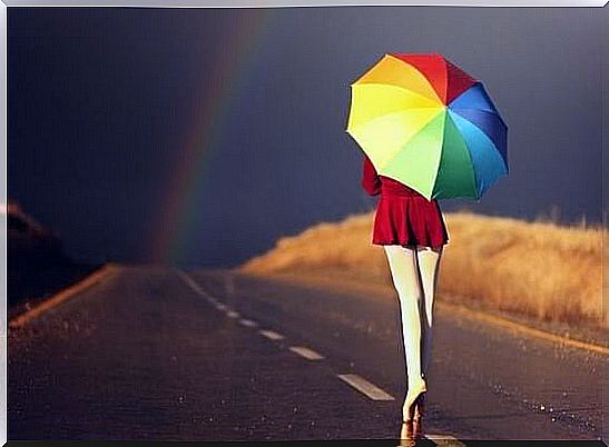 Woman with umbrella walking towards rainbow