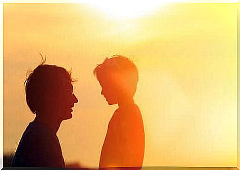 Silhouettes of man talking to son in front of the sun