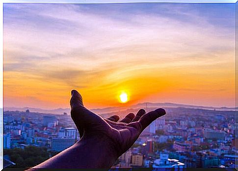 A hand reaches out towards a sunset as a symbol that one must appreciate what one has